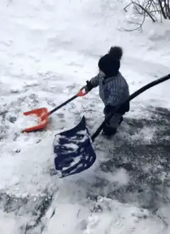Toddler shoveling snow with adult help