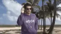 Man in purple hoodie adjusting sunglasses on beach