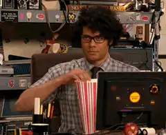 Richard Ayoade eating popcorn at desk