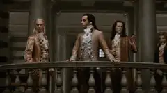 Three men in 18th century coats on a balcony