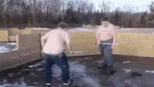 Two shirtless men sword fight in mud