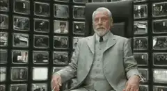The Watcher shrugs in front of monitors