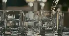 Pouring clear liquid into shot glasses