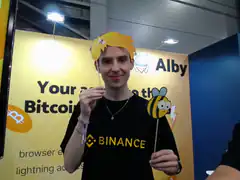 Man at Binance booth with Alby props