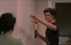 Adam DeVine holding a hammer and waving
