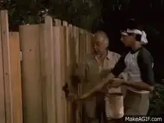 Old man paints fence while young boy watches