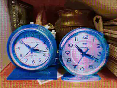 Two blue alarm clocks on a shelf