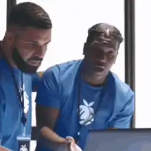 Two men in blue shirts looking at a laptop