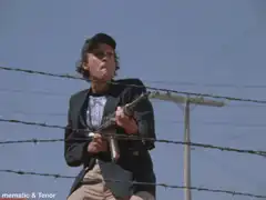 Woman firing a submachine gun behind barbed wire