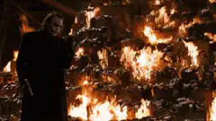 Joker standing in front of burning money