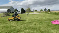 Person on riding mower pulls child in pink sled