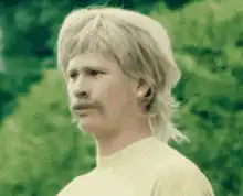 Man with mustache and mullet looking confused