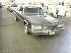 Old car drives with people watching