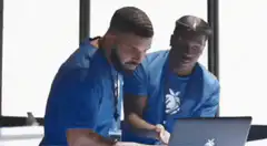 Two men in blue shirts looking at a laptop