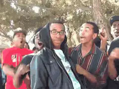 Man with glasses smiles while friends react excitedly