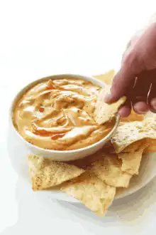 Hand dipping tortilla chip in cheese dip