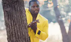 Man in yellow jacket peeking from behind tree