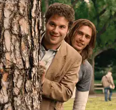 Two men peeking from behind a tree
