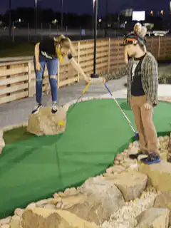 Girl on rock hits golf ball with man's club