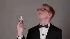 Man in tuxedo sips wine and gestures