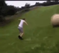 man running from rolling hay bale