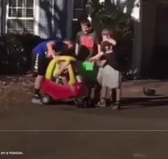 Kids push toddler in toy car down the street