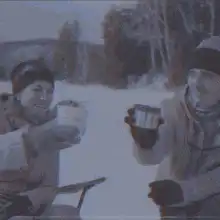 Two people toasting with mugs in the snow