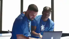 Two men in blue shirts react to laptop