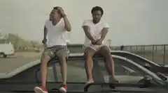 Two men sitting on a car roof dancing