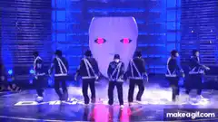 K-pop group dancing on stage with giant face