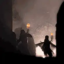 Silhouettes holding torches in a misty cave