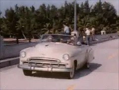 Vintage white convertible driving along coastal road