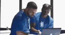 Two men in blue shirts looking at a laptop