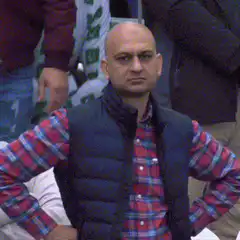Bald man in plaid shirt and vest turns head