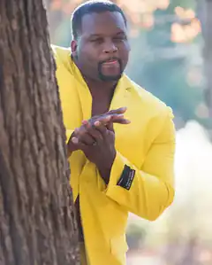 Man in yellow suit rubbing hands by tree