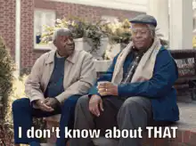 Two older men sitting on a bench, one gestures with a drink