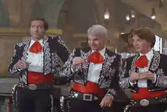 Three men in mariachi suits drink and dance