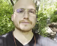 Bald man with glasses smiling in forest