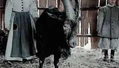Black goat in barn with two children