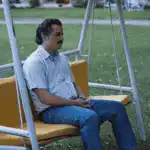 Man sitting on swing and standing by wall