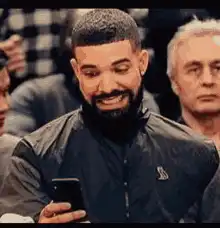 Drake looking at phone and smiling