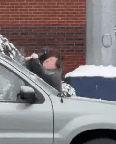 Woman scrapes ice off car windshield