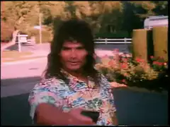 Man in Hawaiian shirt points at camera