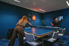 two women playing ping pong in blue room