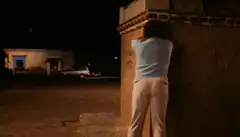 woman peeing against wall at night