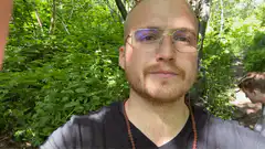 Bald man with glasses smiling in forest
