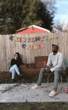 Two people sitting under existential crisis sign