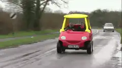 Two men driving a red and yellow toy car