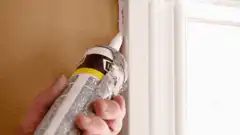 Hand applying caulk to window frame