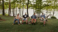 Four men sit in chairs by a lake
